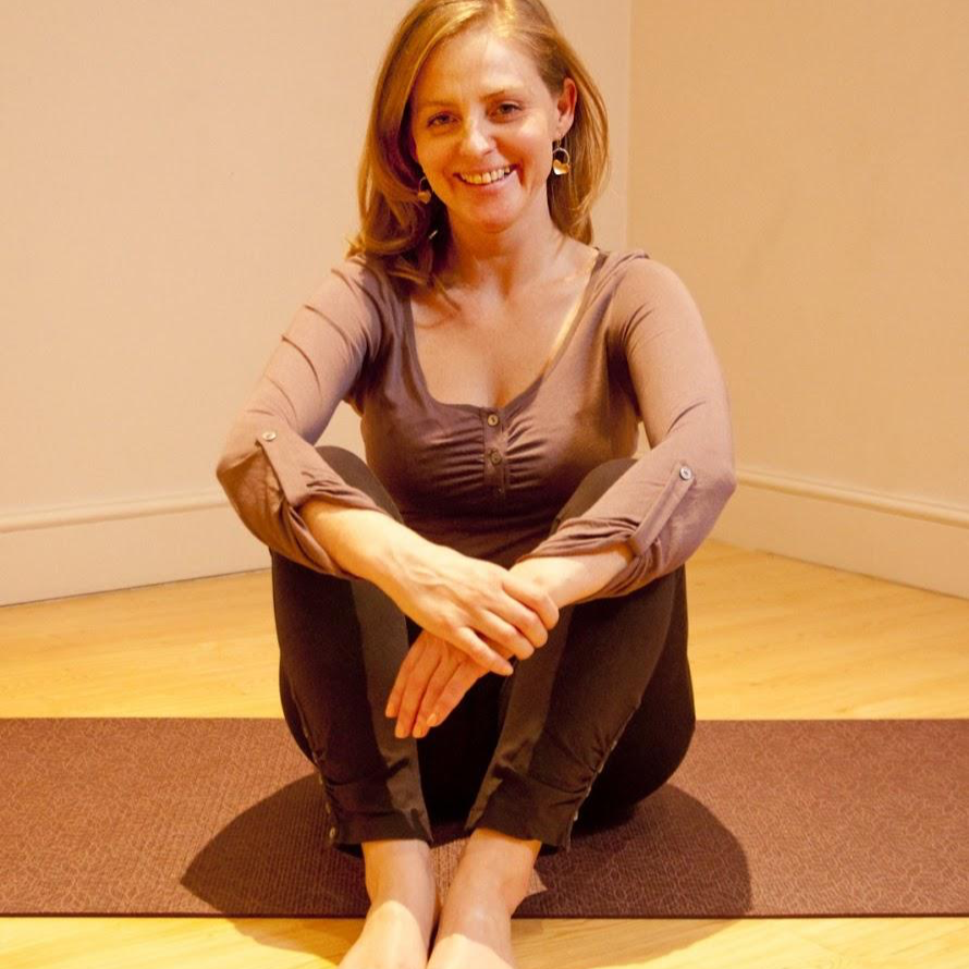 Amy Ku Redler seated cross-legged on a mat, smiling