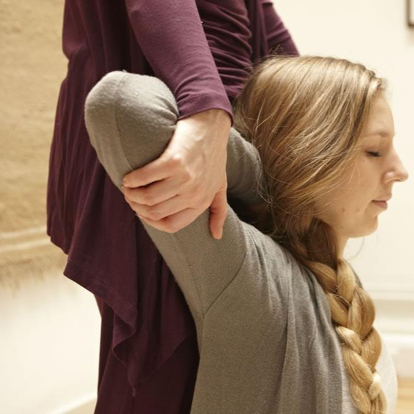 Amy standing behind a seated client, lifting and stretching their arm overhead