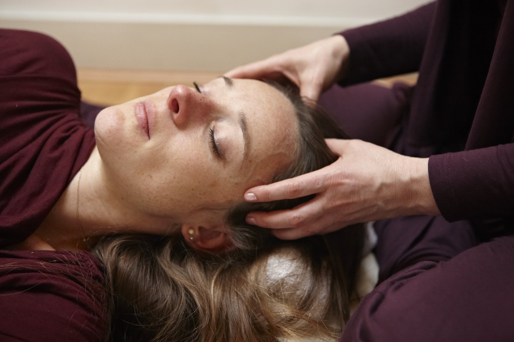 Amy's hands cradling the back of a client's head as they lie with their eyes closed