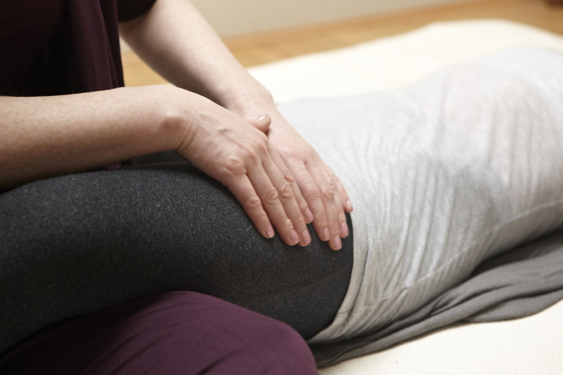 Two hands resting on the hip and lower back of a client lying on their side